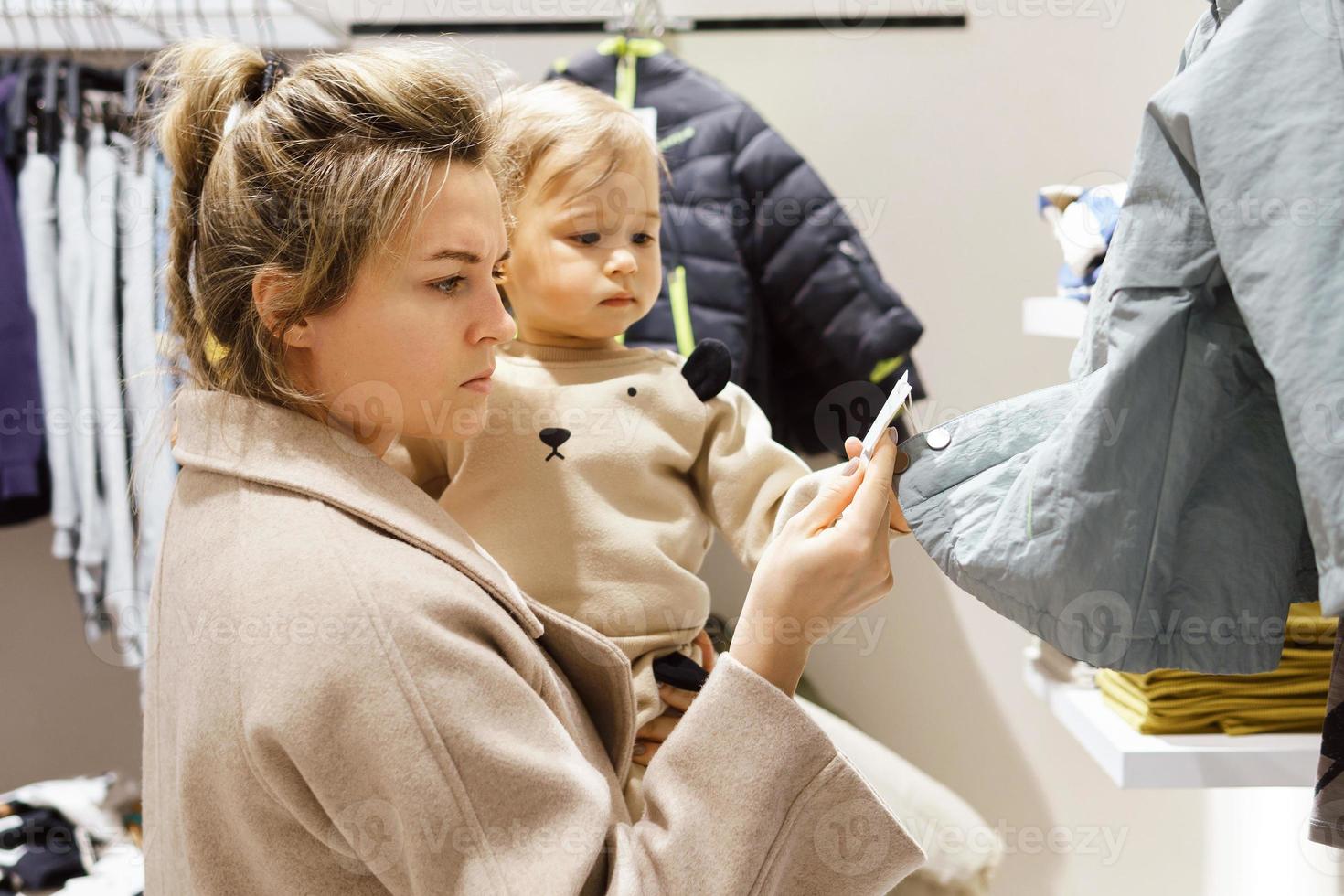 Woman with her baby son choosing clothing in clothes store photo