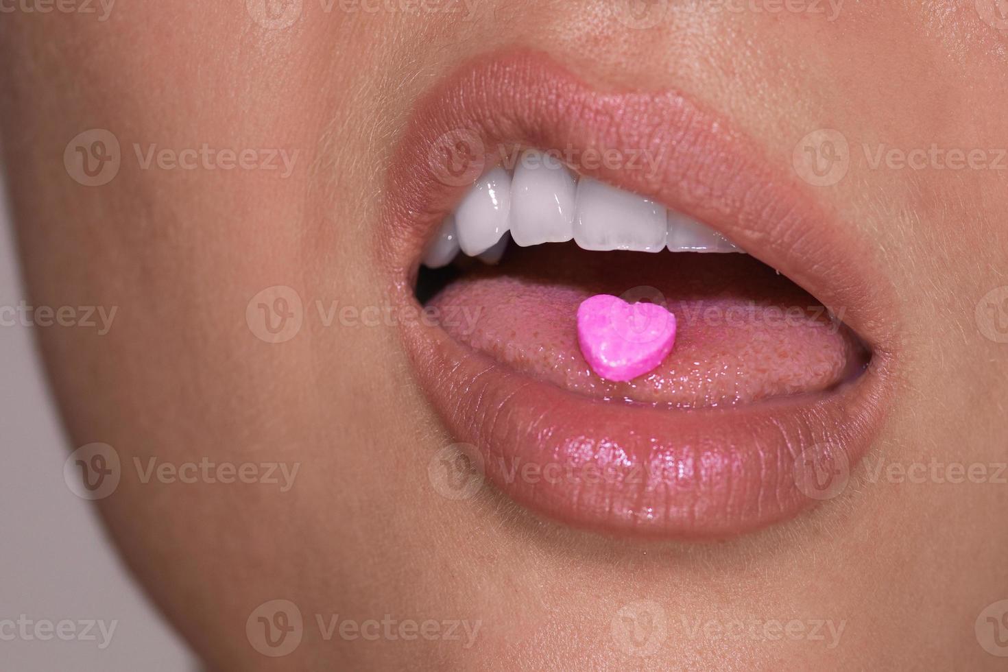 Half of female face with heart shaped pill on tongue. photo