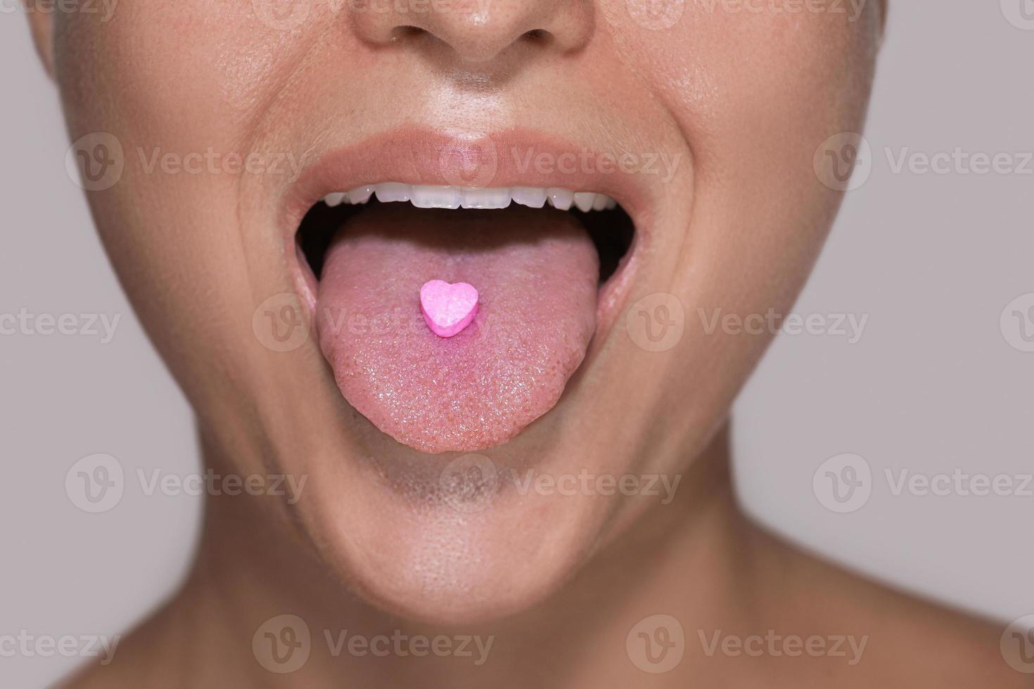 Half of female face with heart shaped pill on tongue. photo