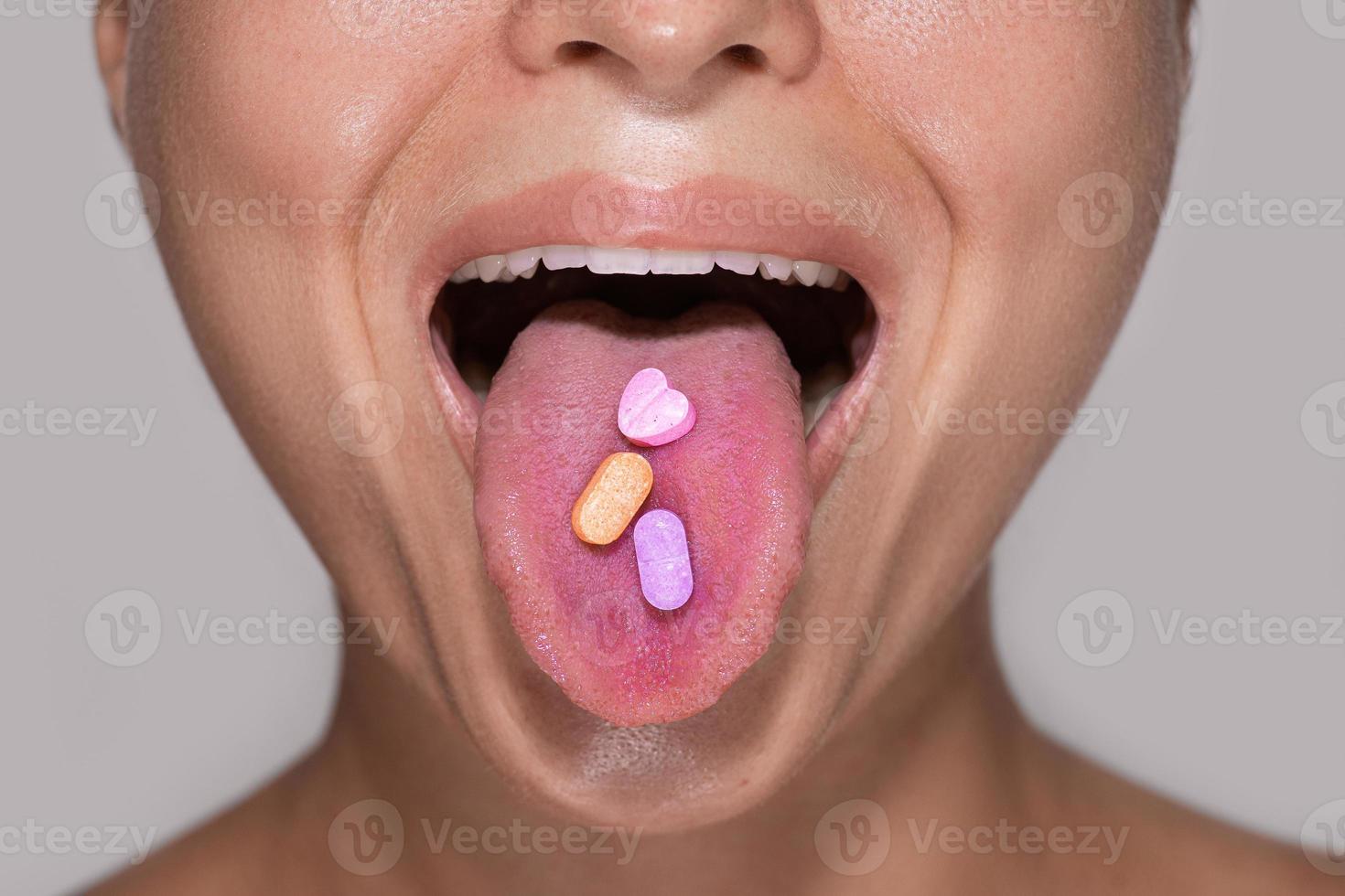 Half of female face with colorful pills on tongue. photo