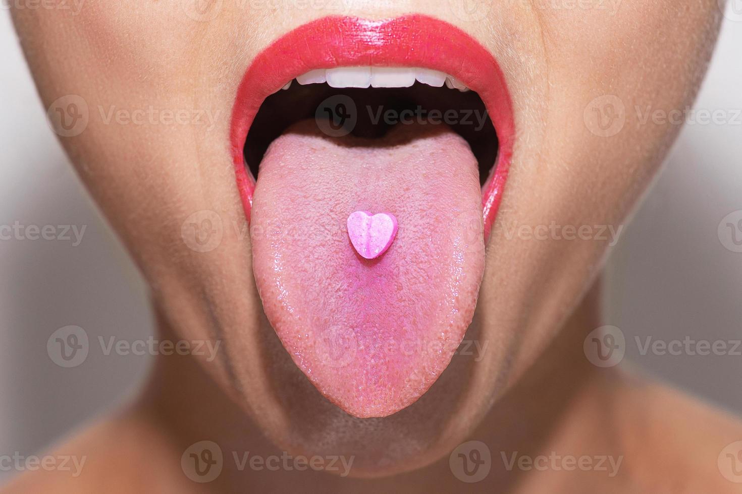 Half of female face with heart shaped pill on tongue photo