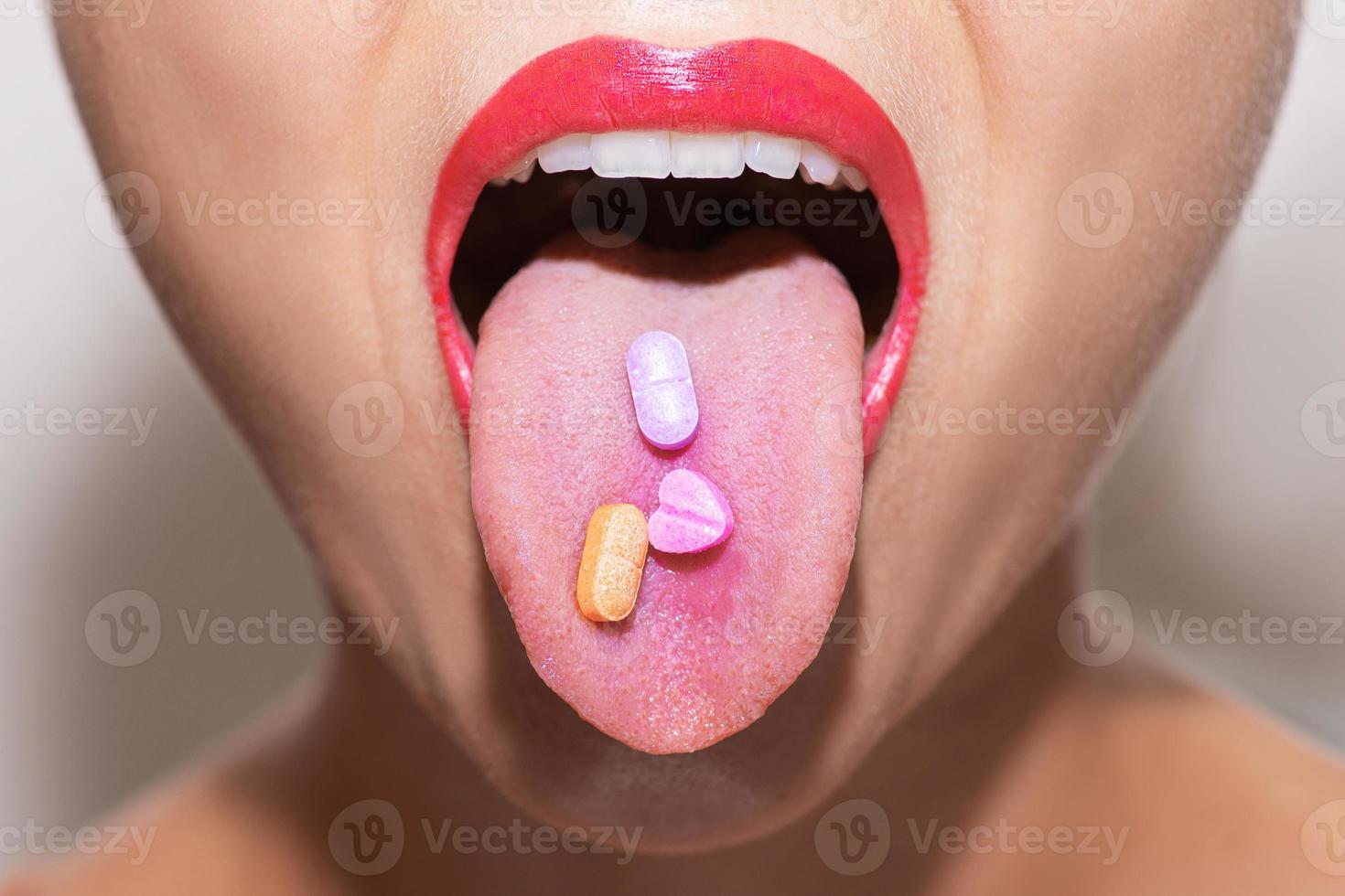 cara femenina con vitaminas coloridas o pastillas de drogas en la lengua foto