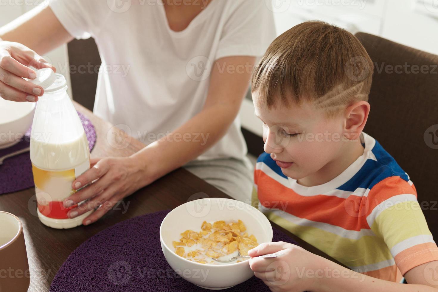 hermosa madre y su lindo hijo comiendo copos de maíz saludables para el desayuno foto