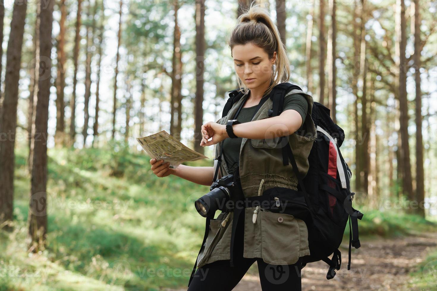 Female hiker with big backpack using map for orienteering in the forest photo
