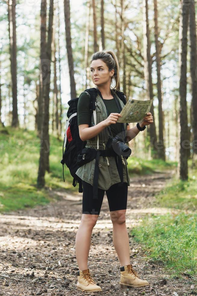 Female hiker with big backpack using map for orienteering in the forest photo