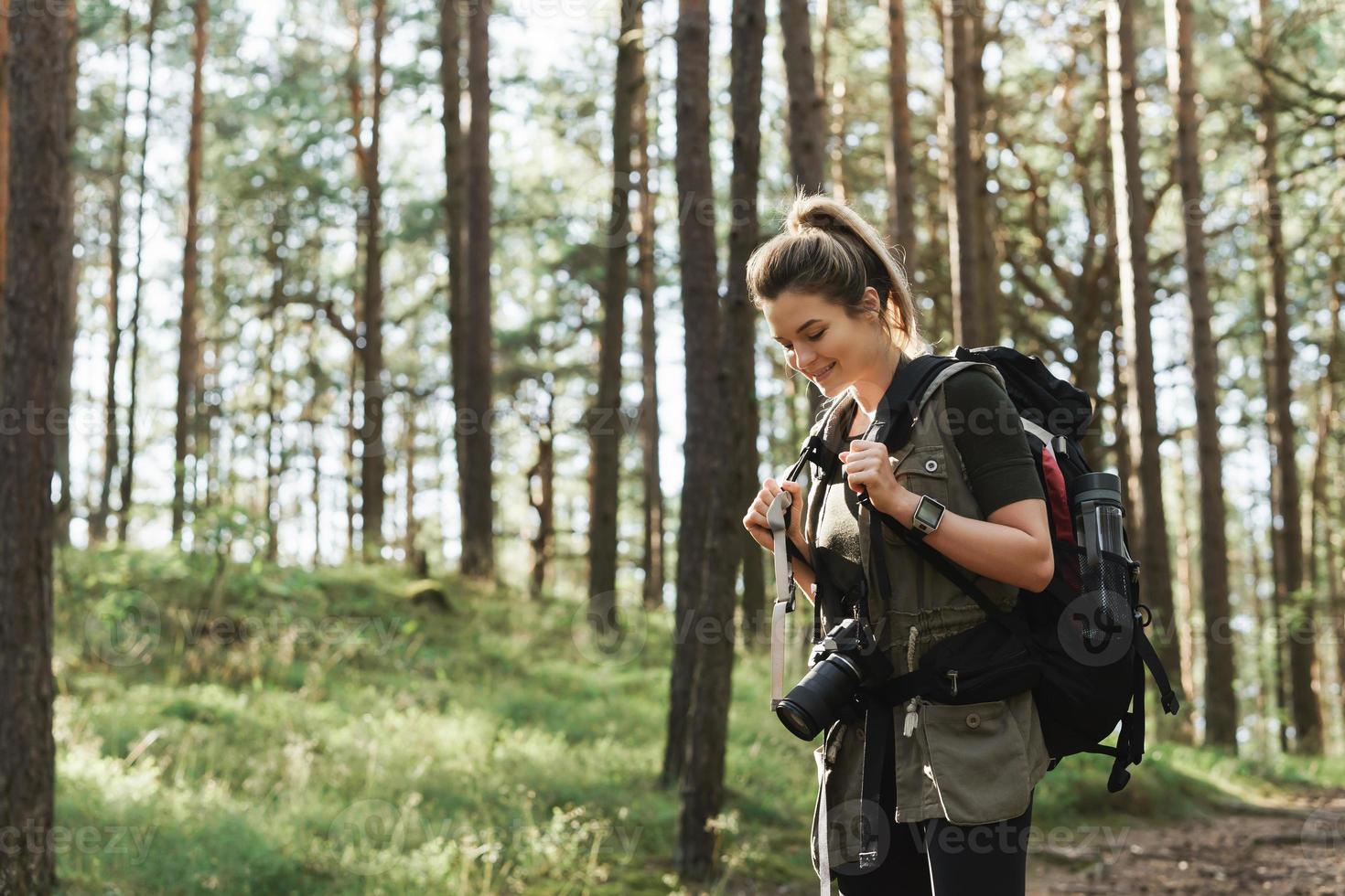 Hiker walking with a backpack and modern mirrorless camera in green forest photo