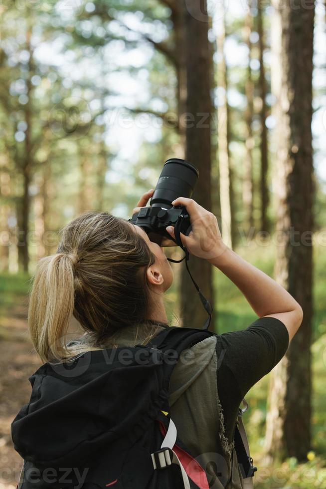 excursionista tomando fotos usando una cámara sin espejo moderna en un bosque verde