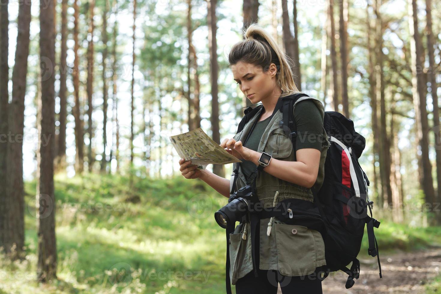 Female hiker with big backpack using map for orienteering in the forest photo