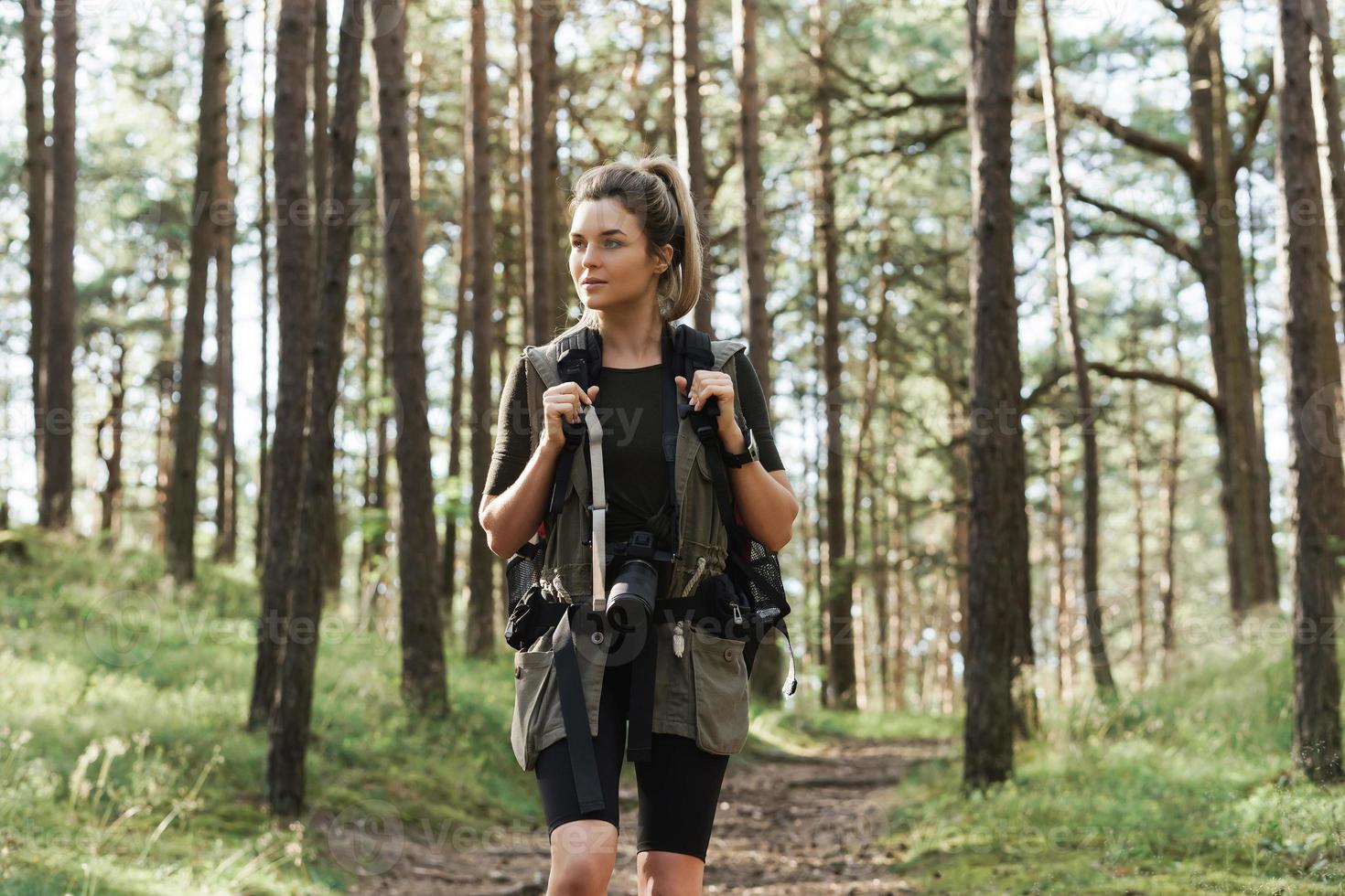 Hiker walking with a backpack and modern mirrorless camera in green forest photo