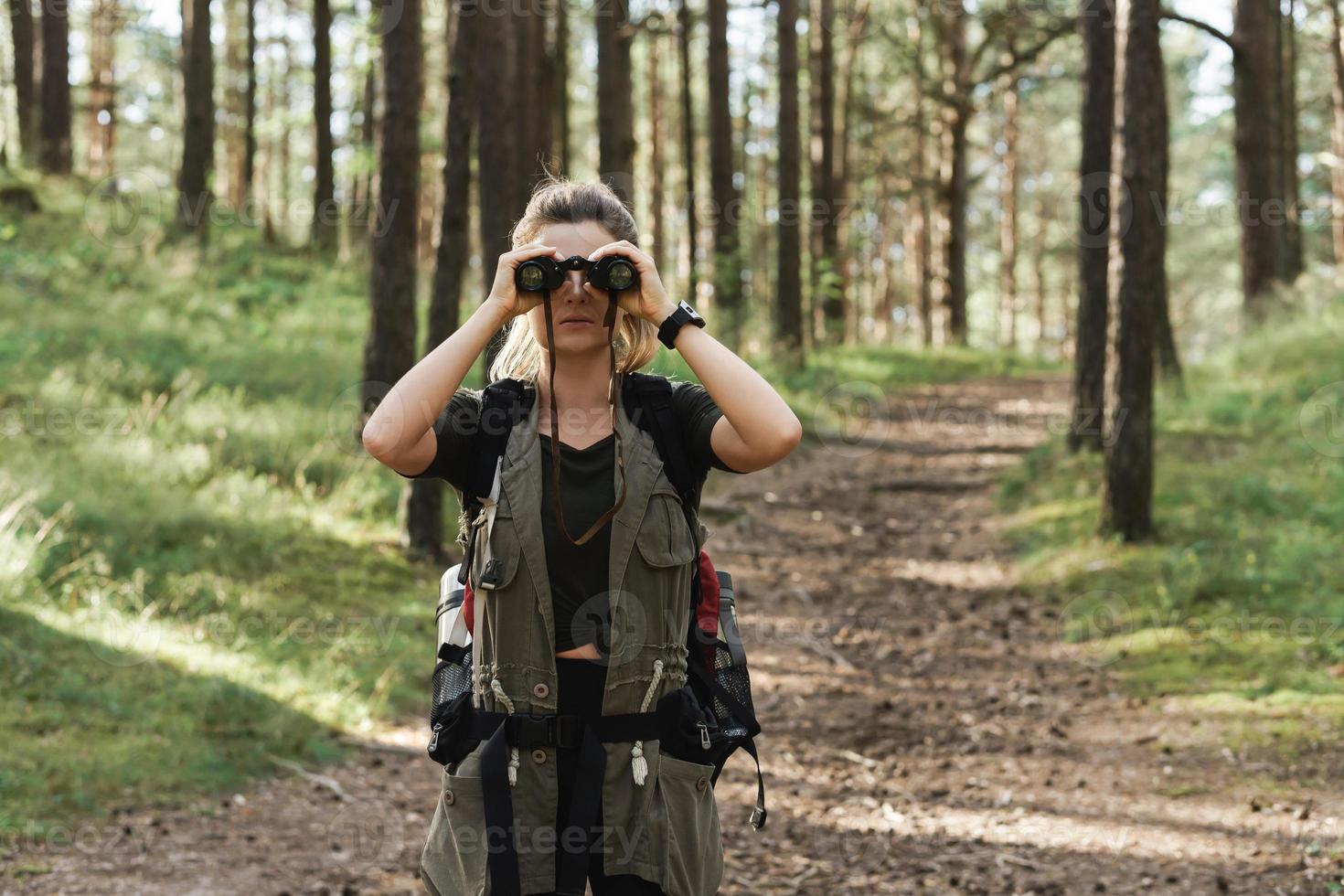 Female hiker is using binoculars for bird watching in green forest photo