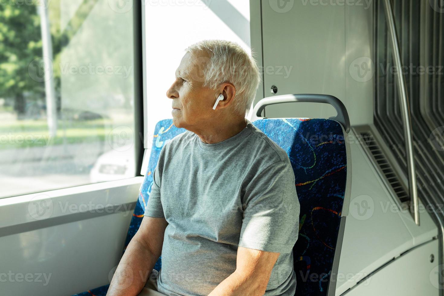 Elderly man is using wireless earbuds during ride in public transport photo