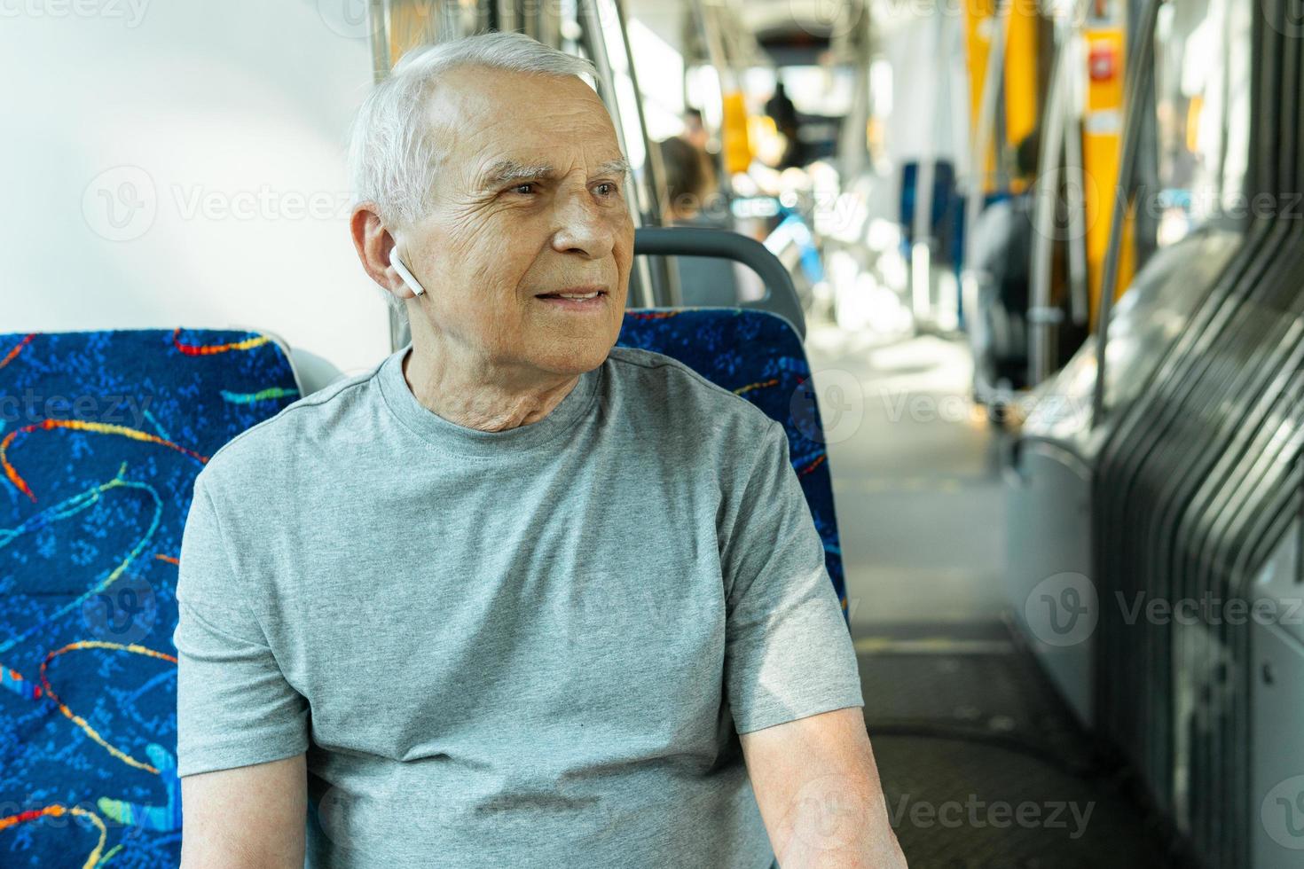 Elderly man is using wireless earbuds during ride in public transport photo