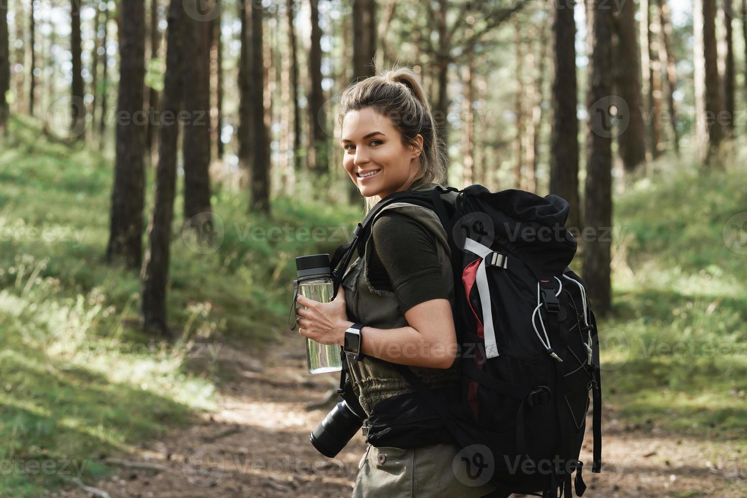 Female hiker with big backpack and reusable bottle for water in green forest photo