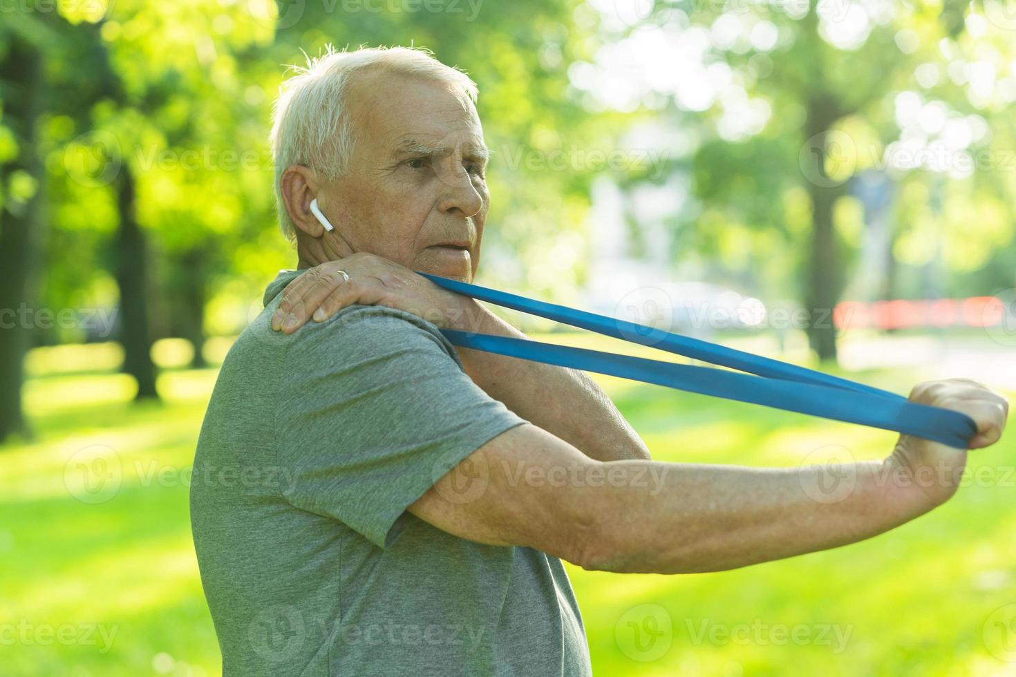 Active elderly man exercising with a rubber resistance band in green city park photo