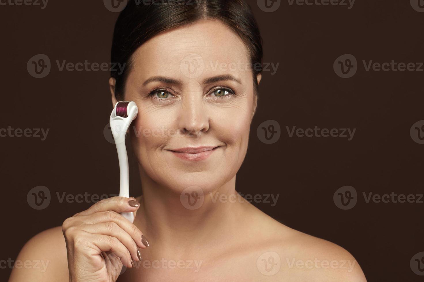 Middle aged woman using mesoroller for her facial skin. photo