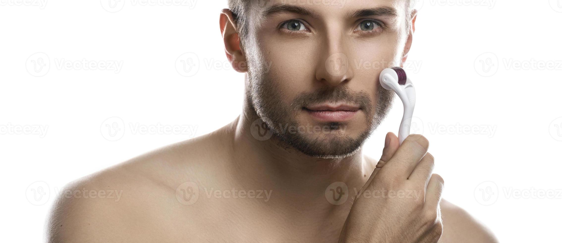 Young handsome man is using derma roller for beard growth photo