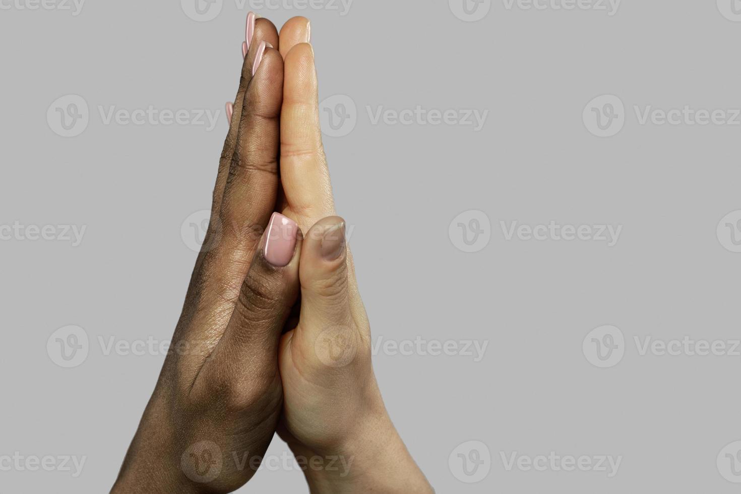 A high five gesture between African and Caucasian women. Closeup of palms on gray background. photo