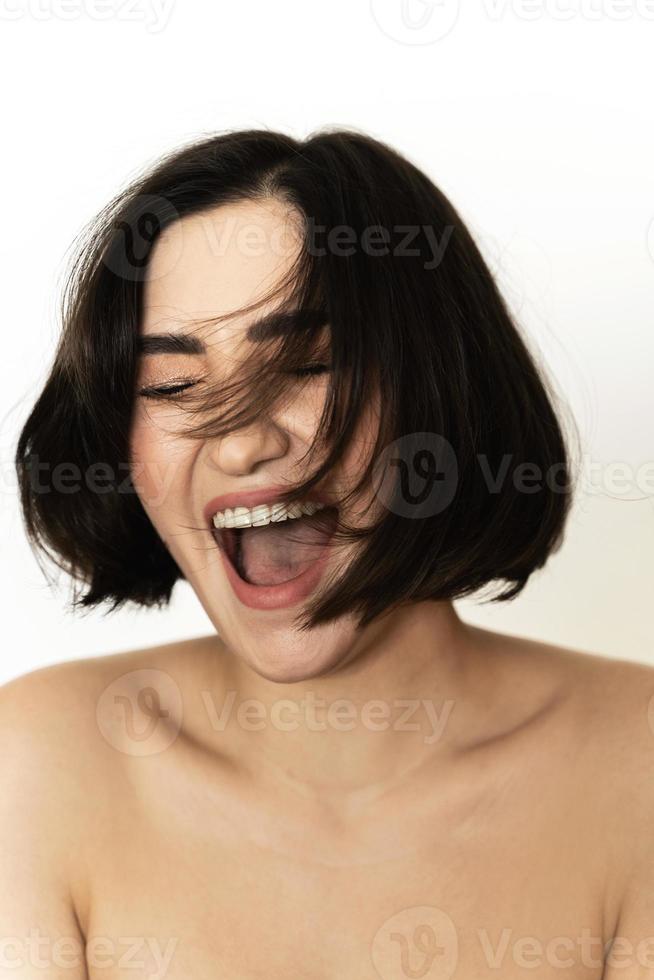 Carefree and happy brunette. Young woman with flying hair is laughing against white background. photo
