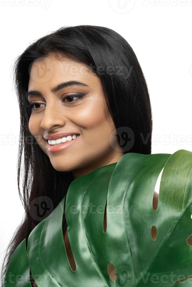 hermosa mujer india con una piel suave sosteniendo una hoja tropical verde foto