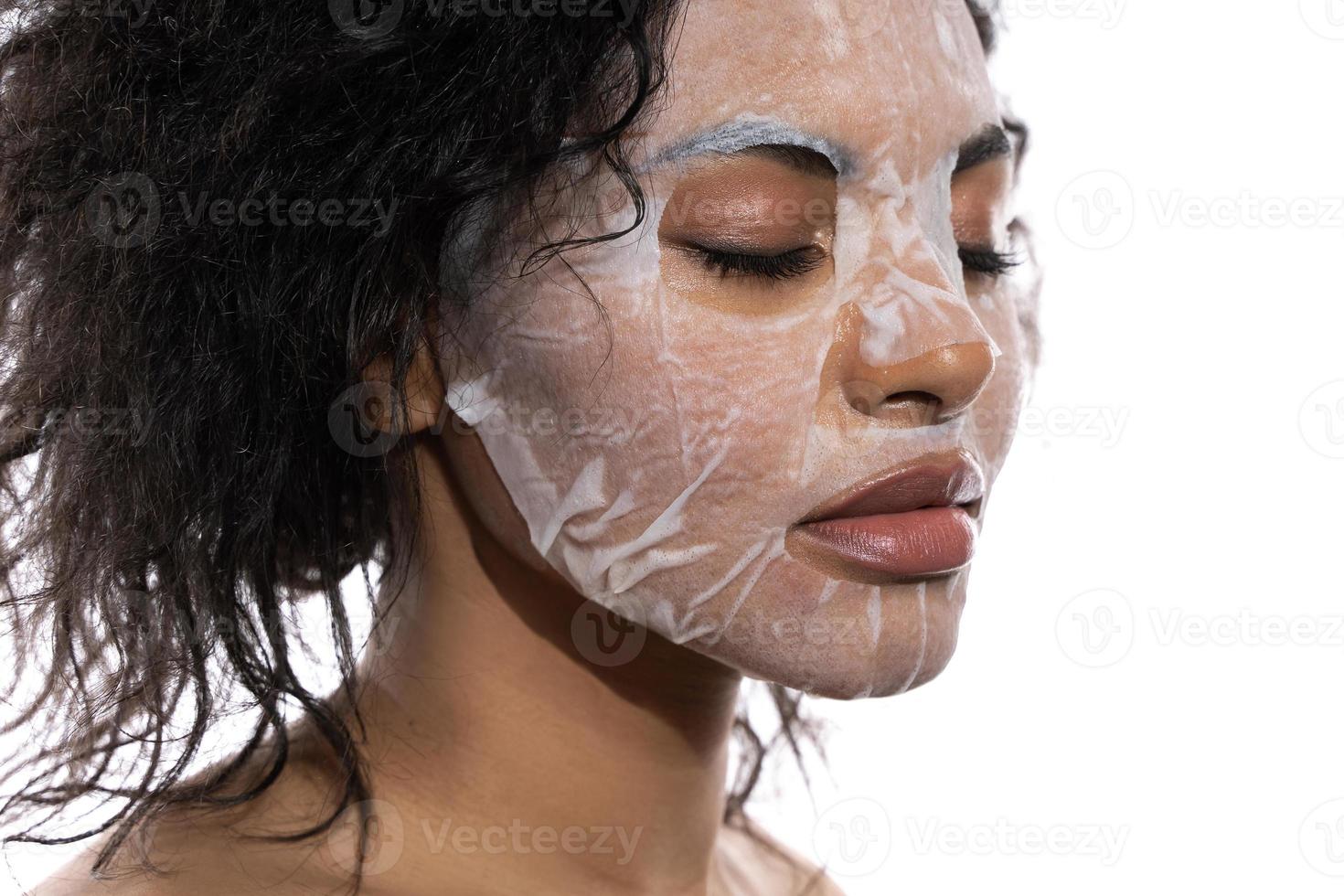 Beautiful black woman with a smooth skin applying facial sheet mask photo