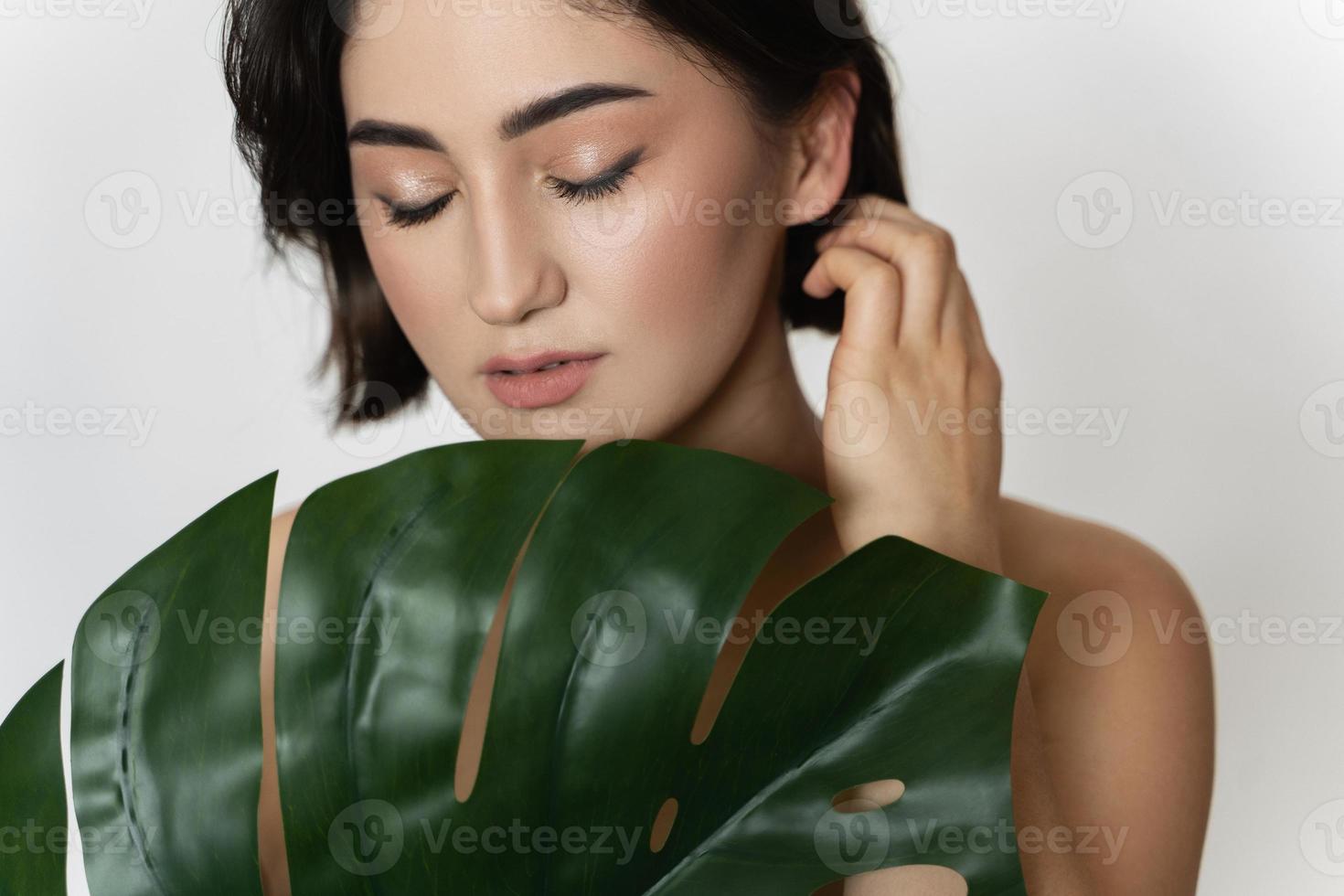 Beautiful woman with a smooth skin holding green tropical leaf on white background photo