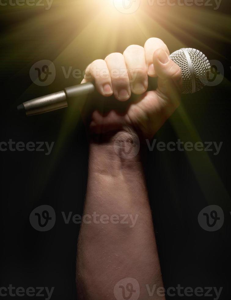 Vertical Microphone Clinched Firmly in Male Fist on a Black Background photo