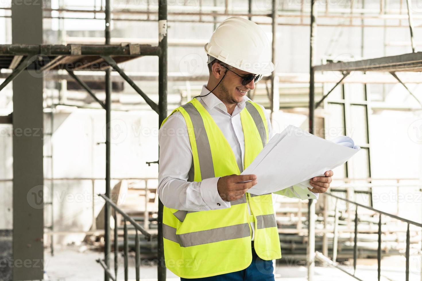 Man architect wearing safety vest with a blueprints on a construction site photo