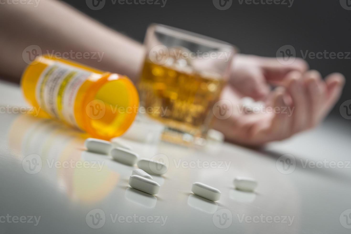 Hand on Ground Behind Scattered Drugs and Glass of Alcohol photo