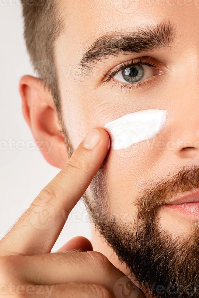Young man is applying moisturizing and anti aging cream on his face photo
