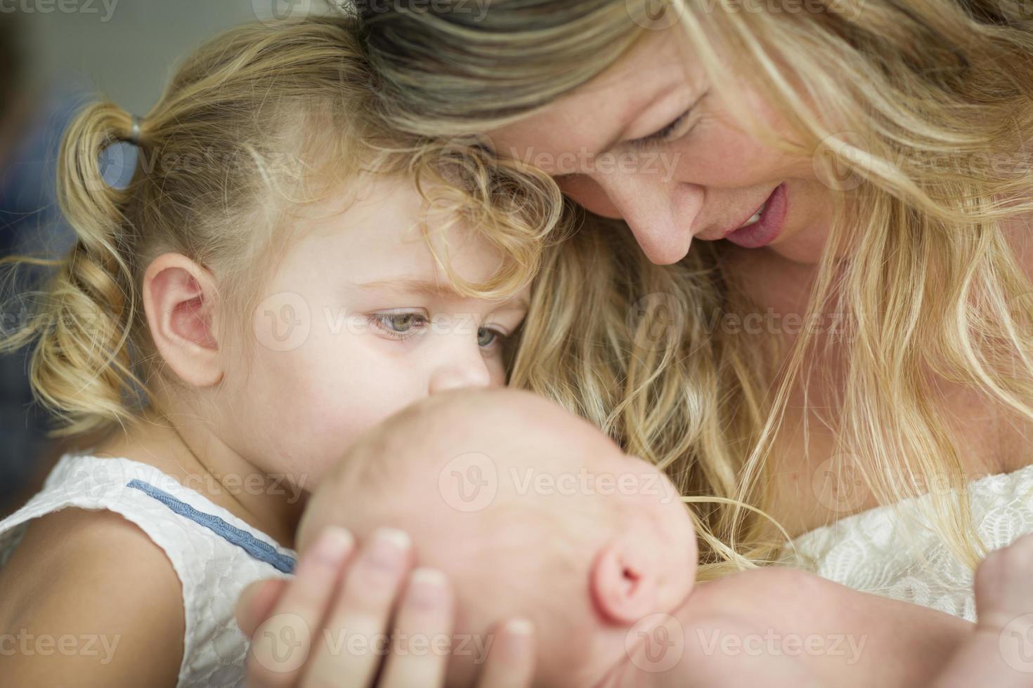 Young Mother Holds Newborn Baby Girl as Young Sister Looks photo