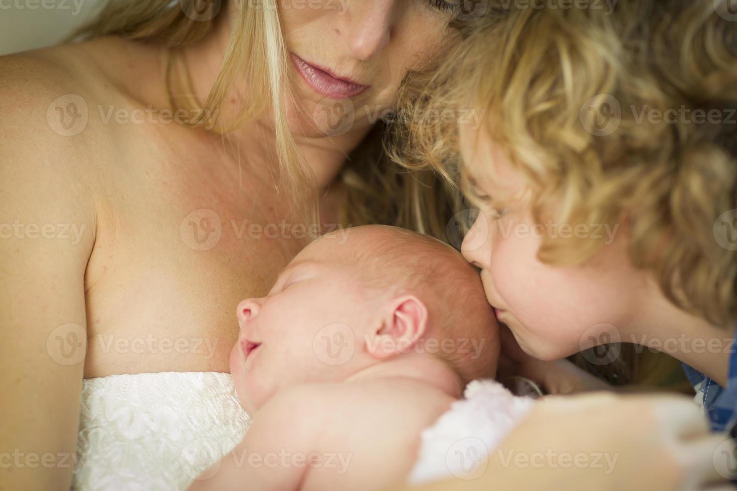 joven madre sostiene a una niña recién nacida mientras su hermano la besa foto