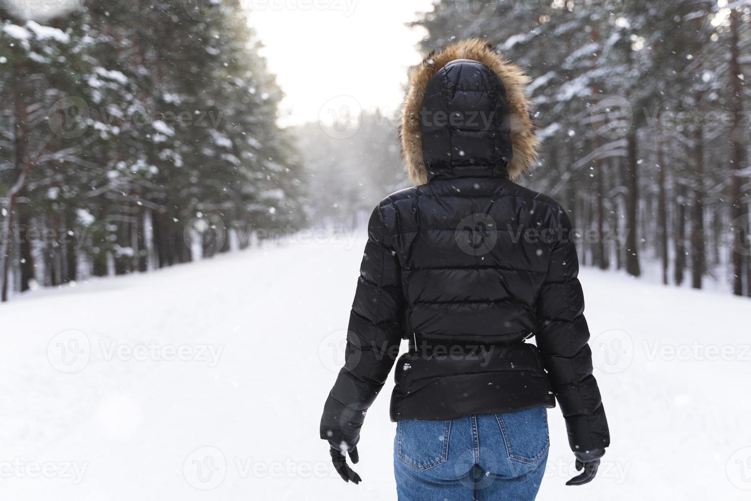 mujer con chaqueta con capucha caminando en el parque durante el frío día de invierno foto