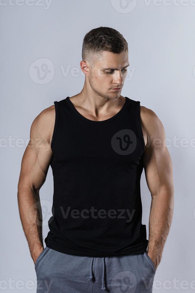 hombre musculoso vestido con una camiseta sin mangas negra en blanco contra un fondo gris foto