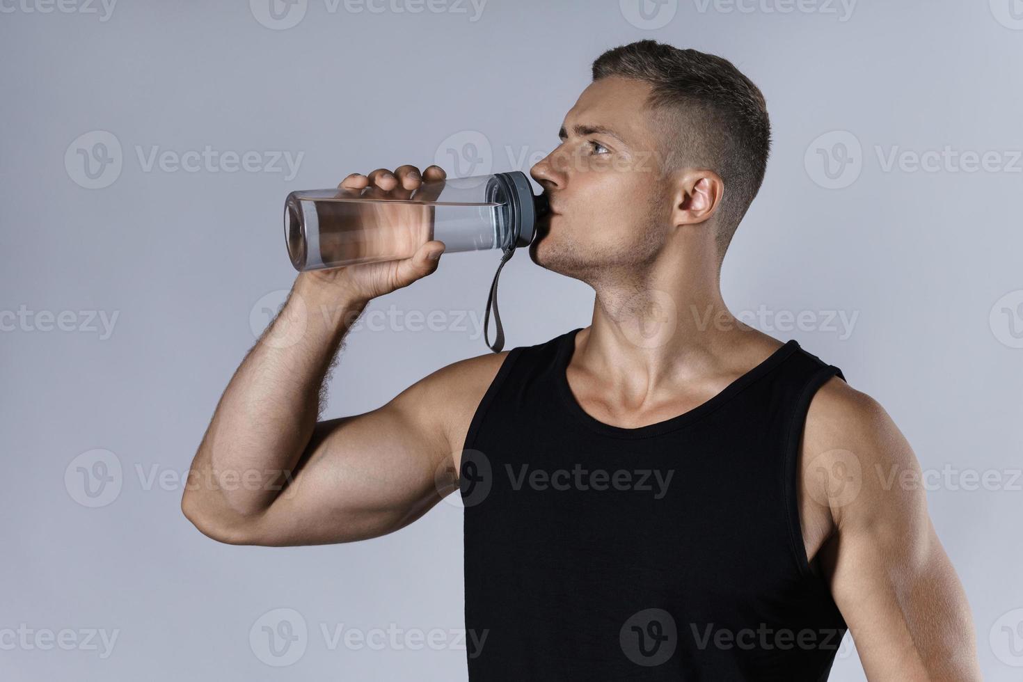 hombre atlético bebiendo agua contra un fondo gris foto