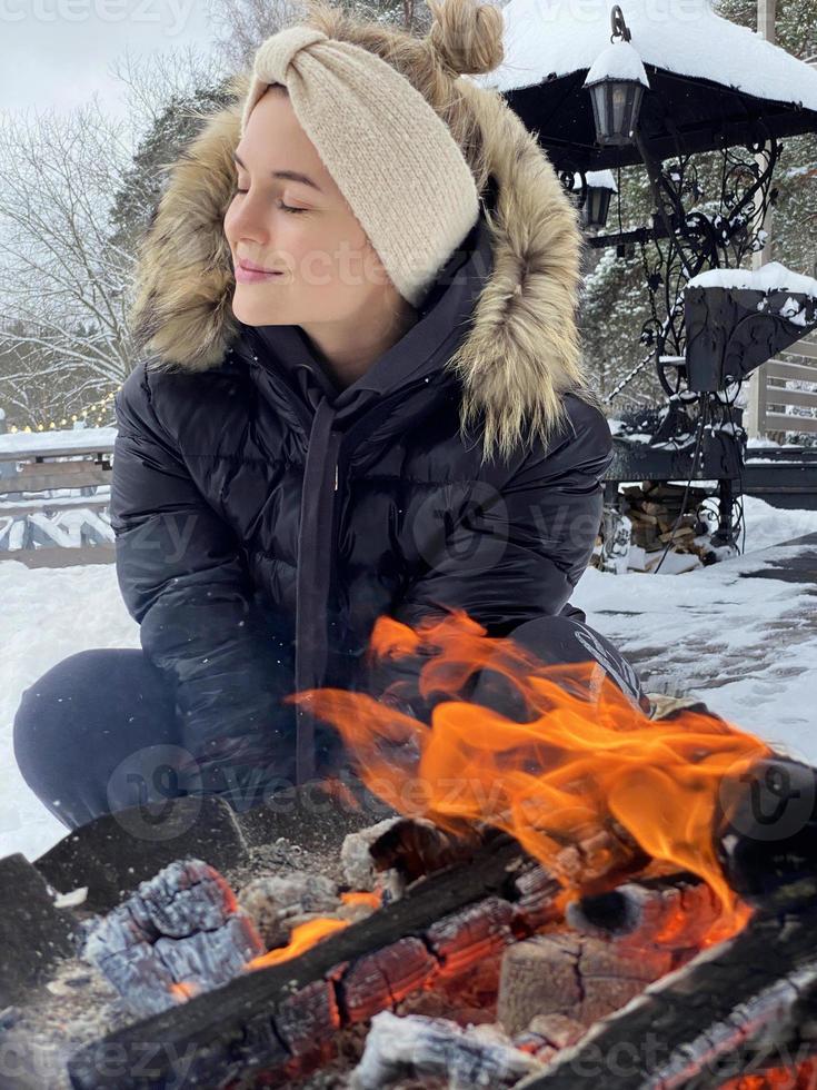 Young woman warming up by the fire pit during cold winter day photo