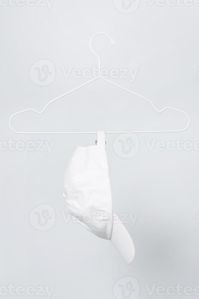 White baseball cap hanging on a hanger against gray background photo