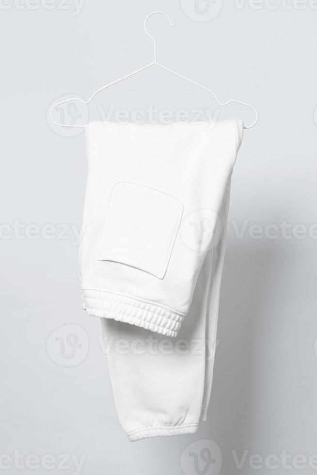 Blank white sweatpants hanging on a hanger against gray background photo