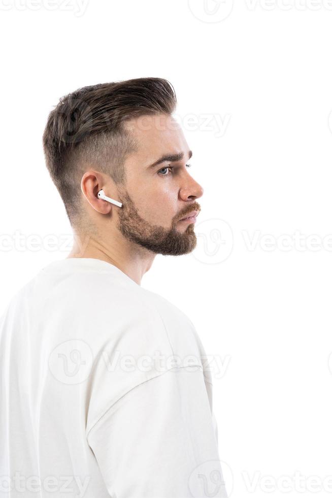 Handsome bearded man in white clothes using wireless earbuds on white background photo