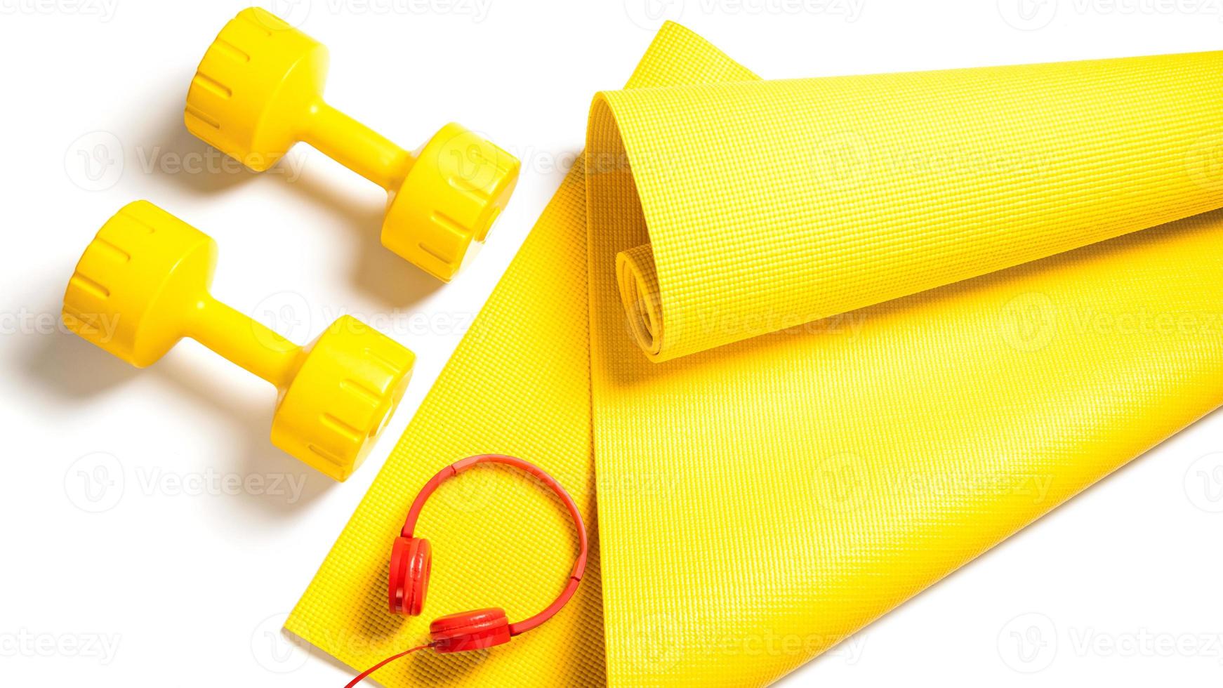 Yellow dumbbells, fitness mat and red headphones on white background photo