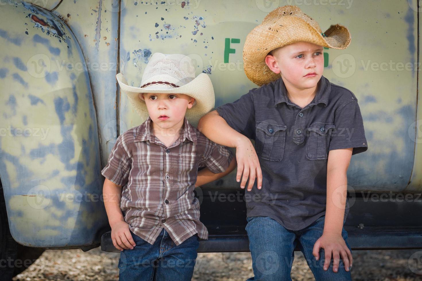 dos jóvenes con sombreros de vaquero apoyados en un camión antiguo en un entorno rústico. foto