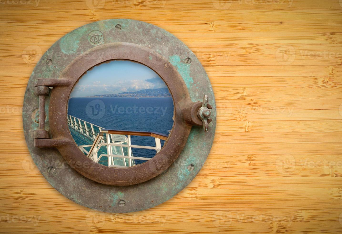 Antique Porthole on Bamboo Wall with View of Ship Deck Railing and Ocean photo