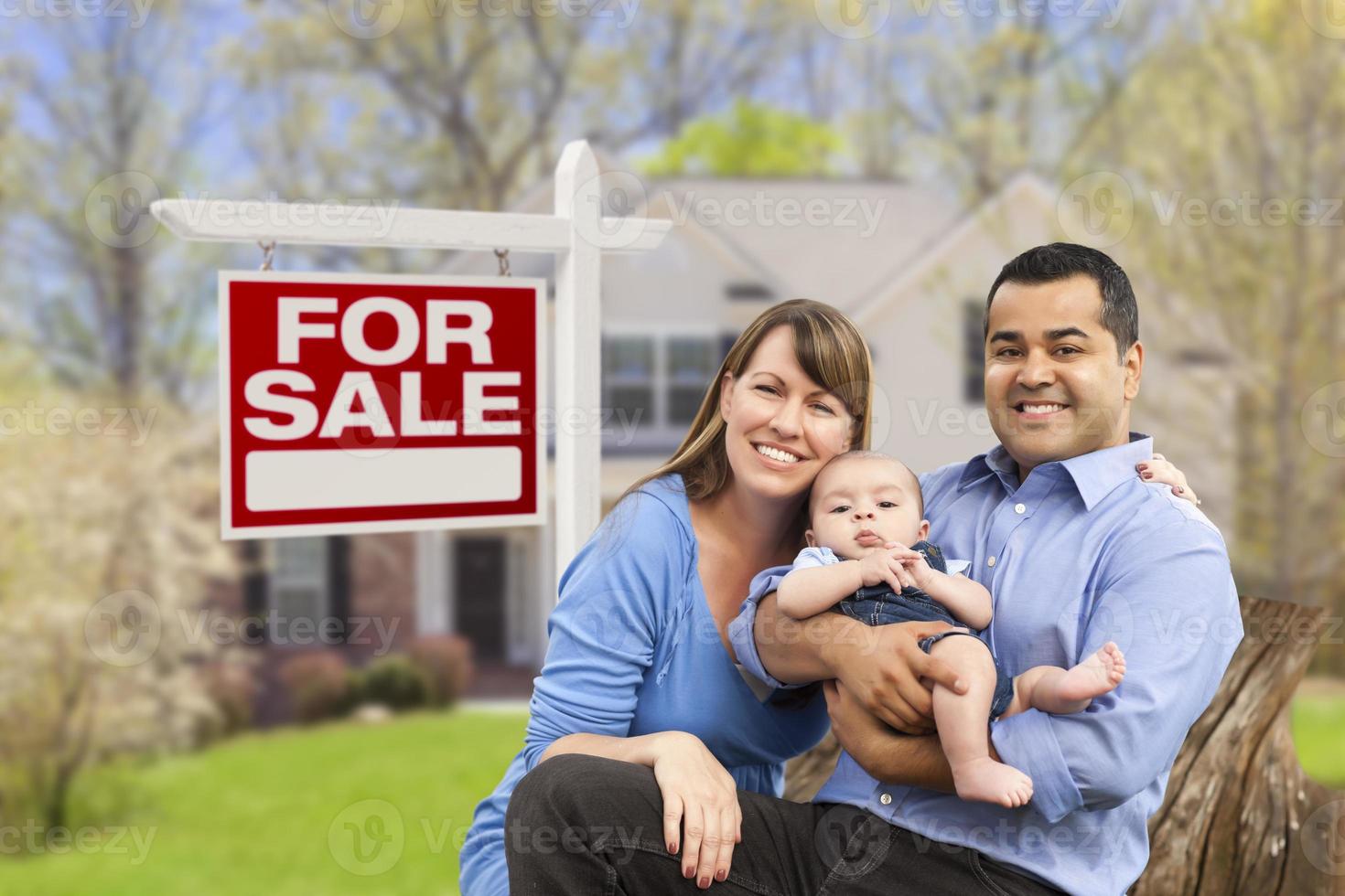 familia joven frente a la casa y el cartel de venta foto