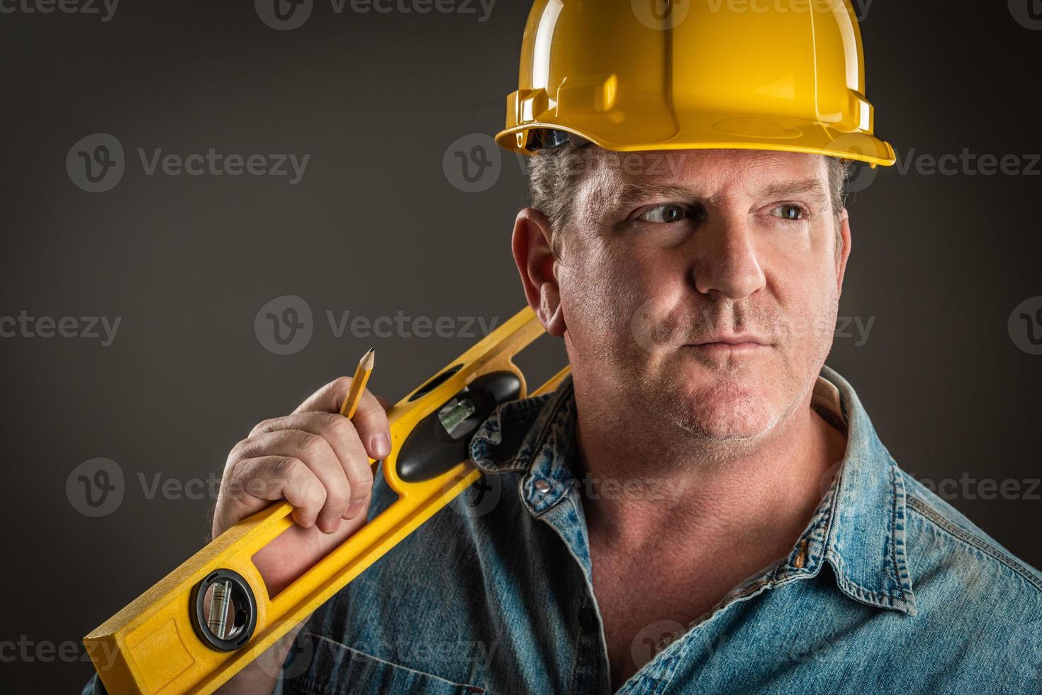 Serious Contractor in Hard Hat Holding Level and Pencil With Dramatic