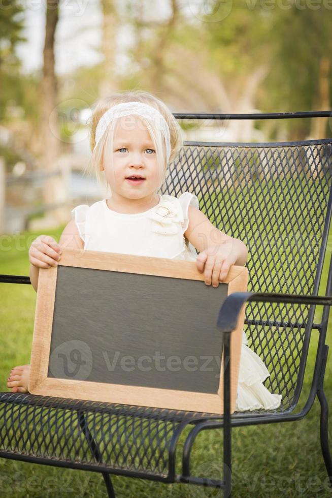 linda niña en una silla sosteniendo una pizarra en blanco foto