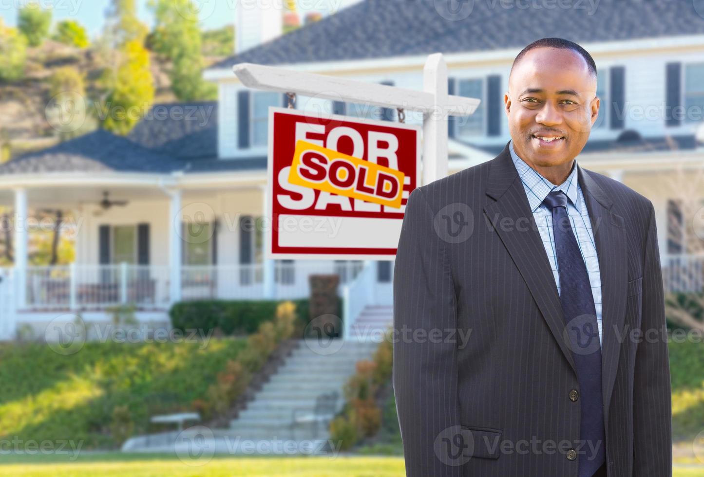 African American Agent In Front of Beautiful Custom House and Sold For Sale Real Estate Sign. photo