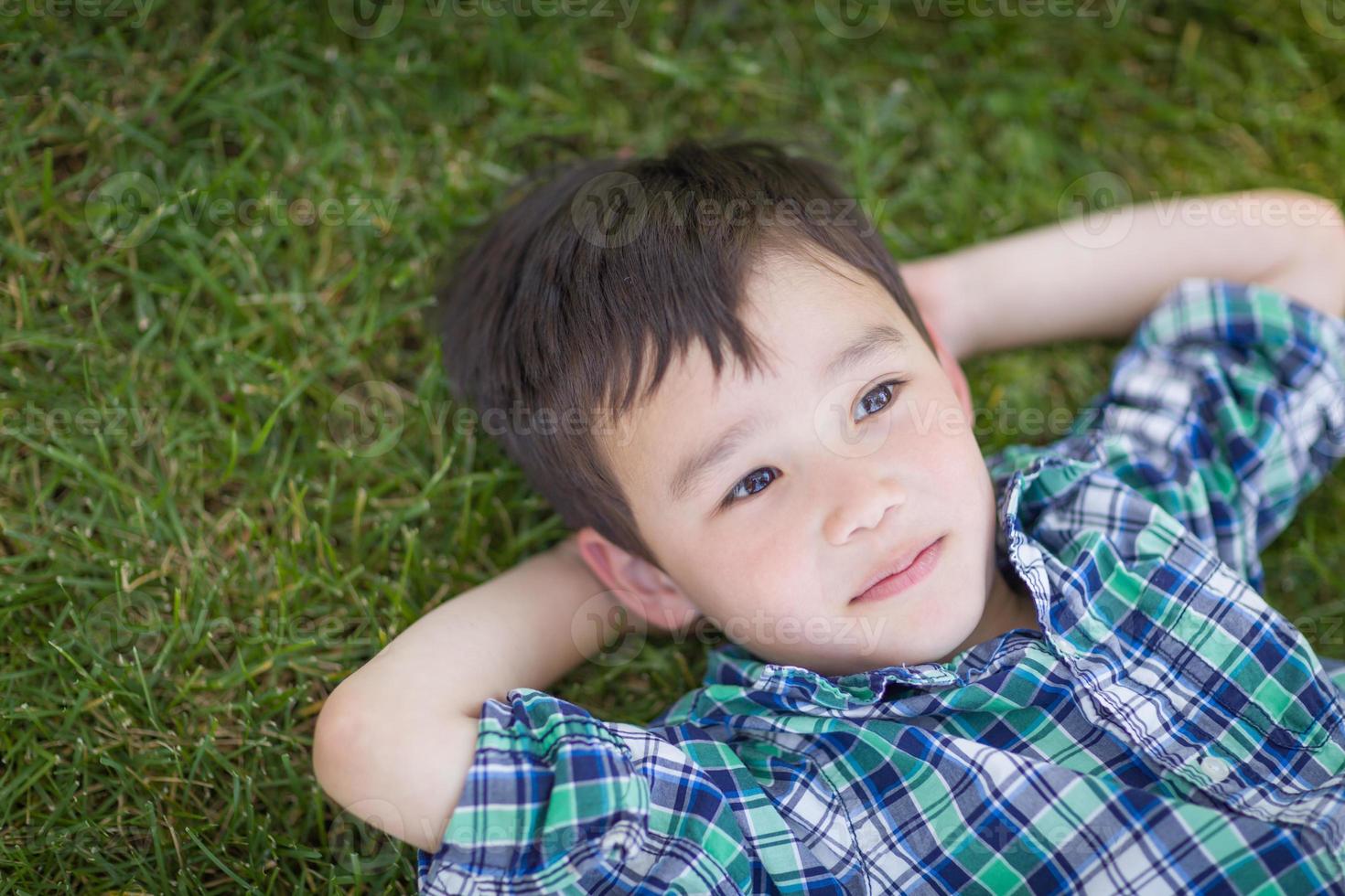un joven chino y caucásico de raza mixta pensativo relajándose en su espalda afuera en la hierba foto