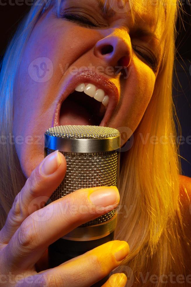 Female vocalist under gelled lighting sings with passion into condenser microphone. photo