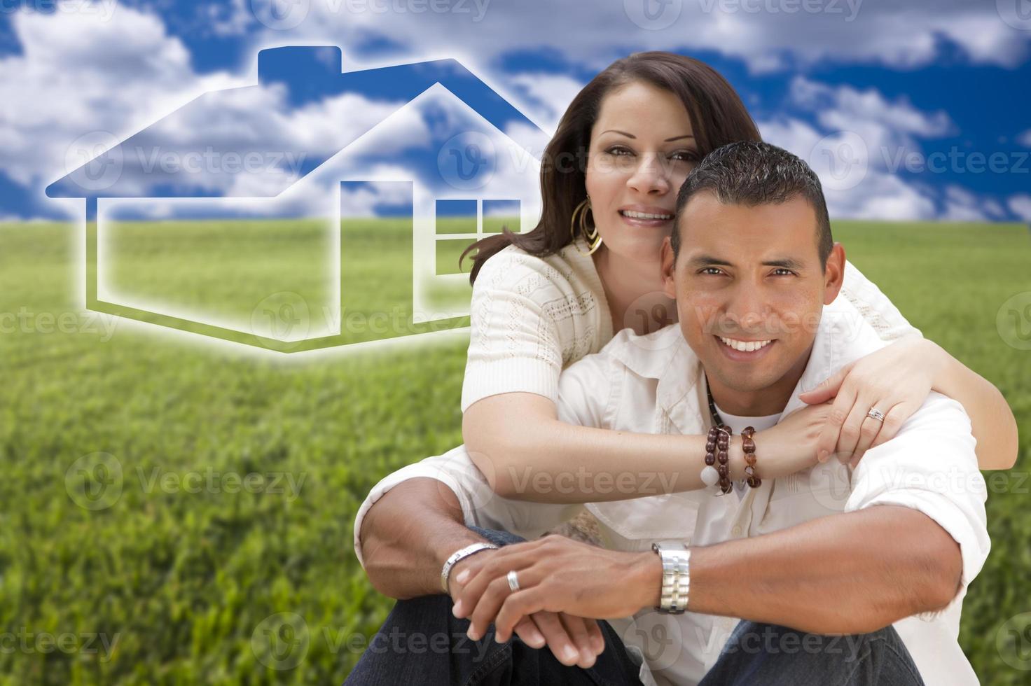 Hispanic Couple Sitting in Grass Field with Ghosted House Behind photo