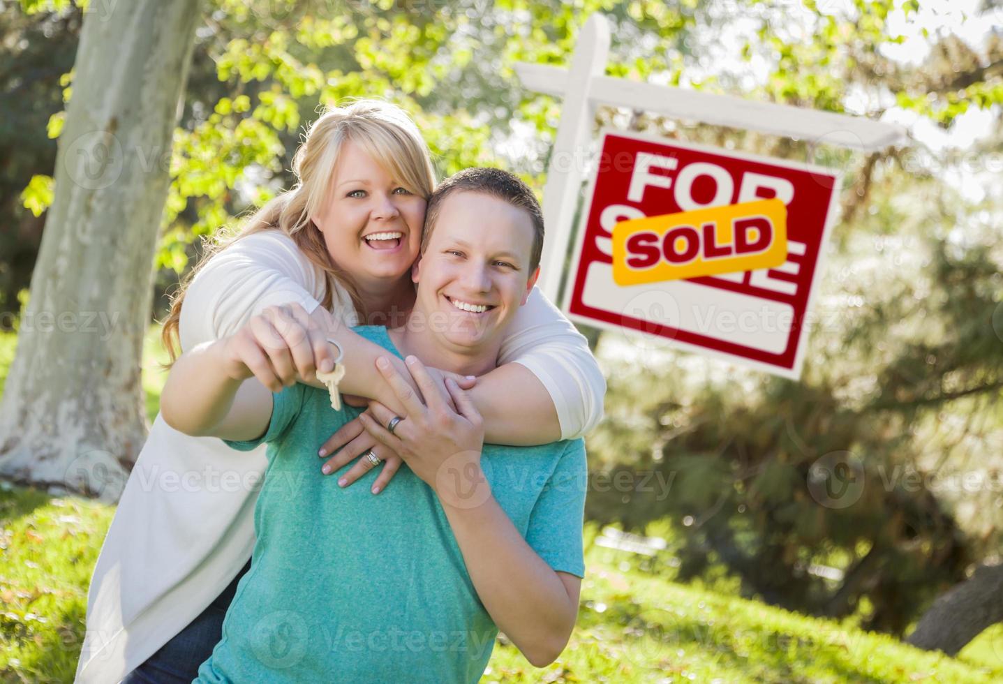 Couple In Front of Sold Real Estate Sign Holding Keys photo