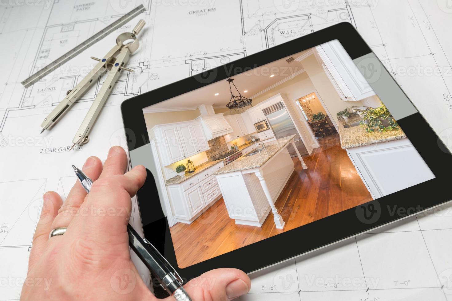 Hand of Architect on Computer Tablet Showing Kitchen Photo Over House Plans